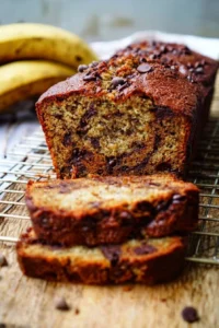 Loaf of chocolate chip banana bread sliced on a wooden cutting board.