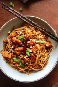 Delicious bowl of Kung Pao Chicken Noodles with vibrant vegetables and peanuts