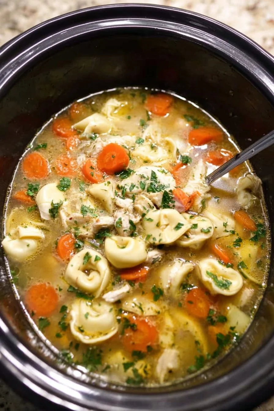 A bowl of slow cooker chicken tortellini soup with fresh herbs on top.