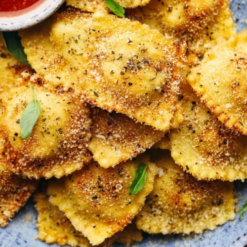 Crispy baked parmesan ravioli served on a plate with marinara sauce.