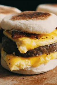 Homemade English muffin breakfast sandwiches stacked with egg, cheese, and bacon.