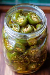 A jar of homemade candied jalapenos on a wooden table.