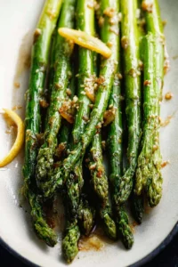 Plate of roasted lemon honey garlic asparagus topped with herbs