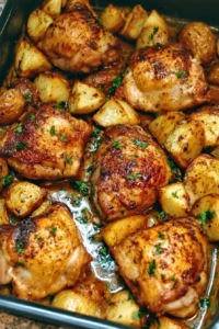 Baked chicken thighs with crispy skin served alongside roasted potatoes