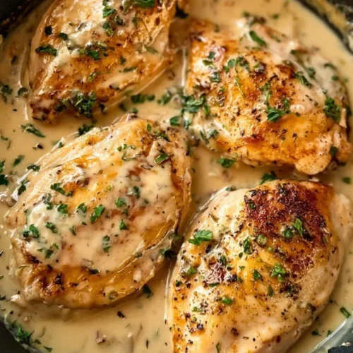 Browned chicken breasts in a skillet with creamy herb sauce