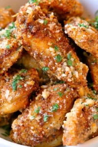 Browned chicken wings topped with grated cheese and chopped herbs