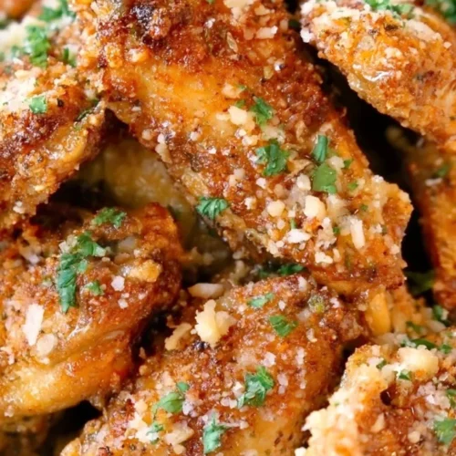 Browned chicken wings topped with grated cheese and chopped herbs