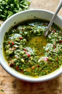 Fresh herbaceous chimichurri sauce in a bowl with herbs and garlic.
