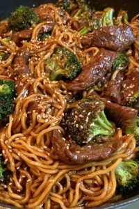 Plate of beef and broccoli lo mein topped with sesame seeds and green onions