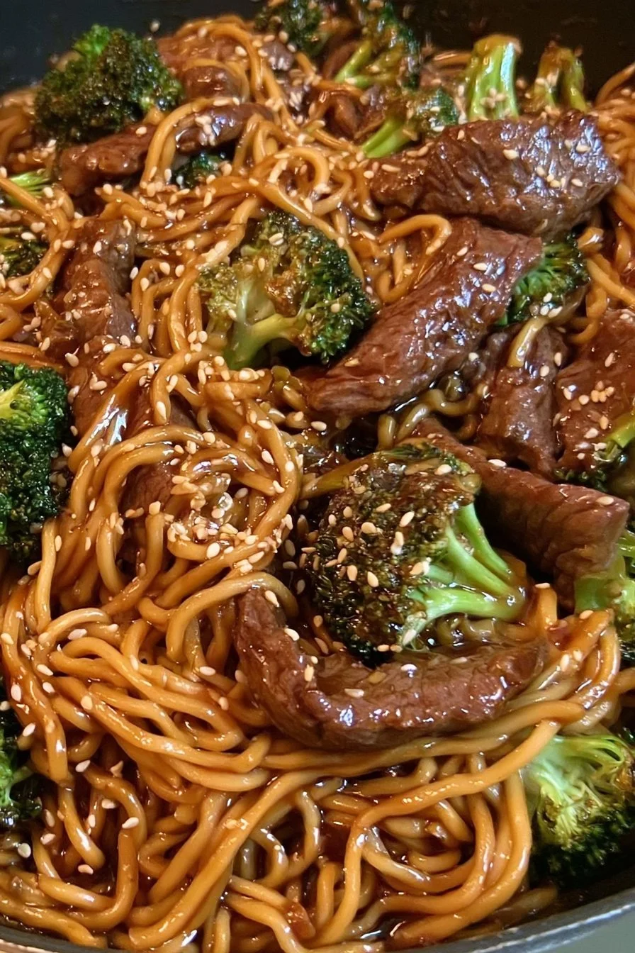 Plate of beef and broccoli lo mein topped with sesame seeds and green onions