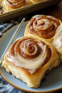 Freshly baked sourdough cinnamon rolls topped with icing on a wooden table.