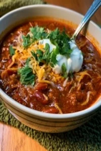 A bowl of the best chili recipe ever, garnished with fresh herbs and cheese