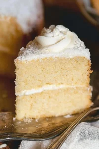 Slice of vintage buttermilk vanilla cake on a plate, topped with frosting.